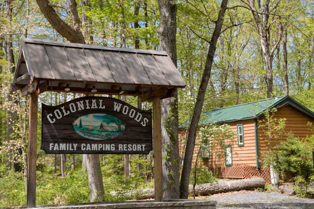 Sign for Colonial Woods Family Camping Resort with a cabin and trees in the background.