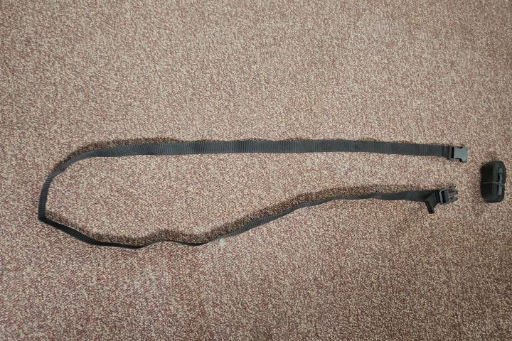 Black adjustable strap with a buckle on a carpeted floor.